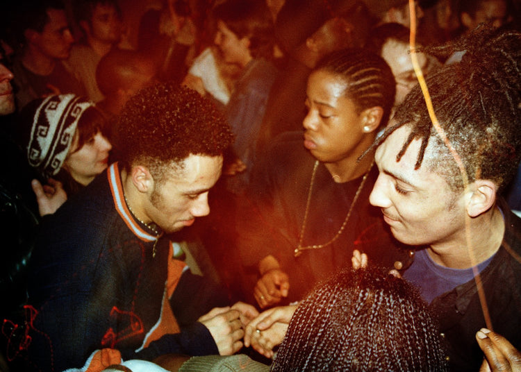 Three men at a nightclub, with a crowd in the background.