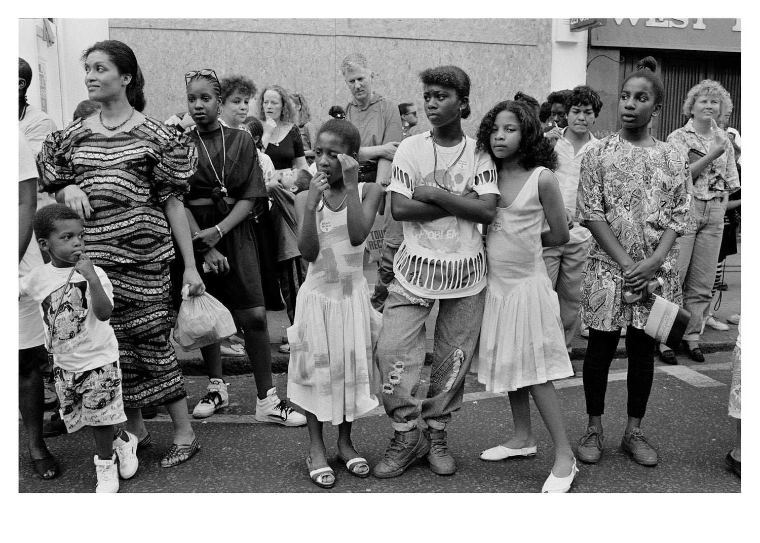 Black and white photo of a group of people, including children, standing on a street at Notting Hill Carnival.