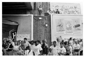 Black and white photo of a crowd gathered outside at Notting Hill Carnival with posters on the wall.