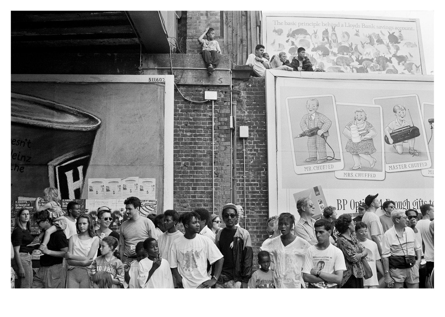 Black and white photo of a crowd gathered outside at Notting Hill Carnival with posters on the wall.