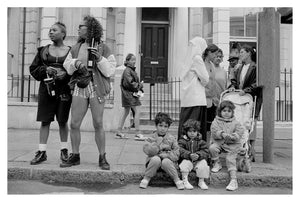 Black and white photo of a group of people and children on a street corner.