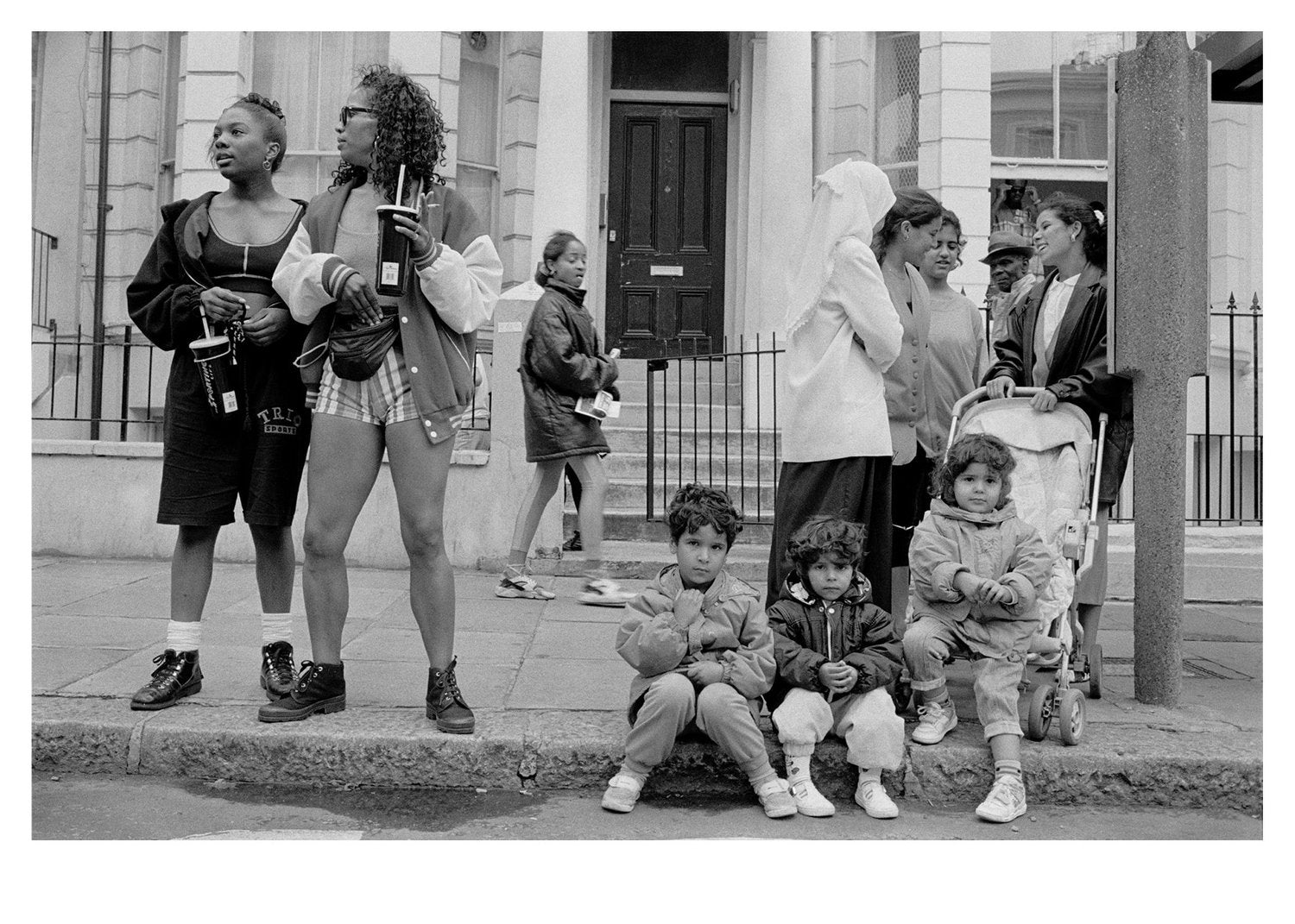 Black and white photo of a group of people and children on a street corner.