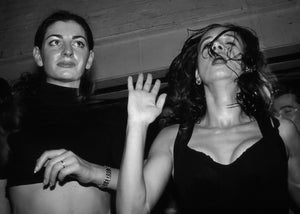 Two women at a party with one raising her hand, black and white photo.