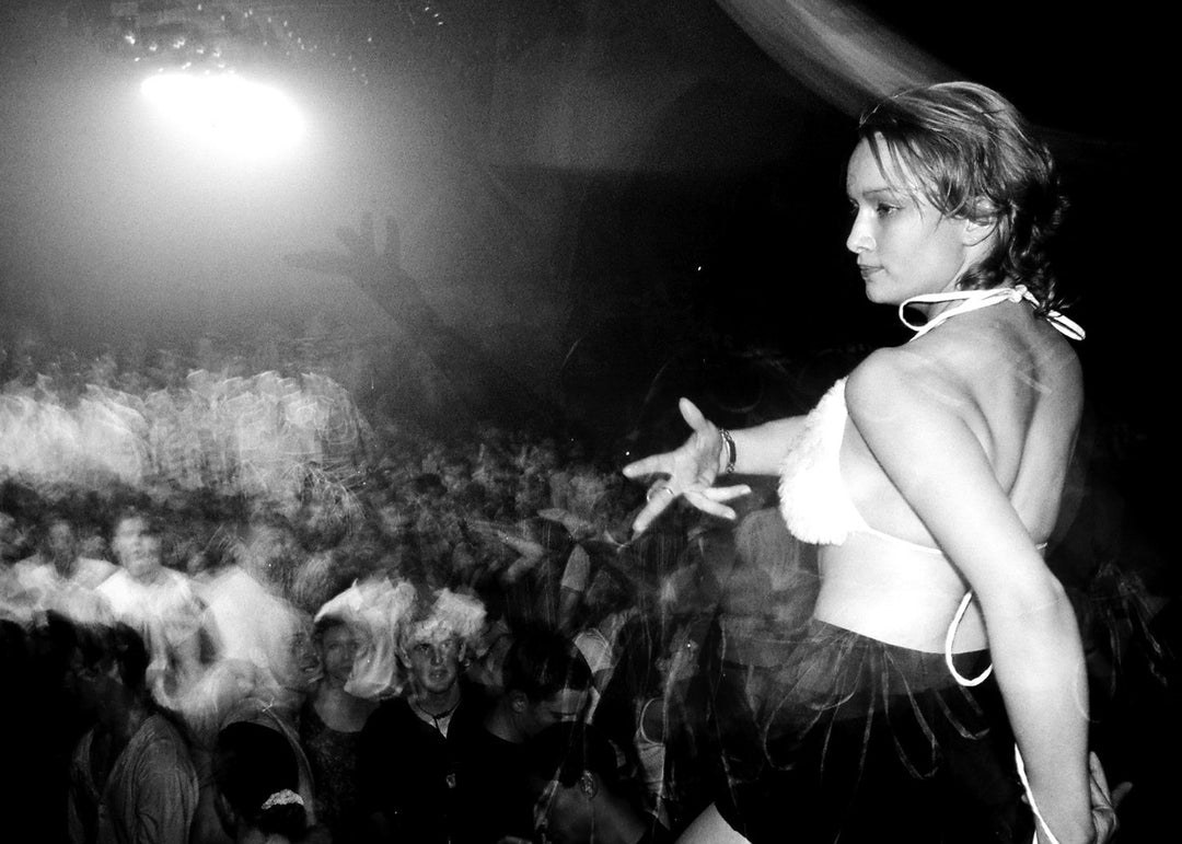 Person on stage in a bikini with a crowd in the background at a rave.