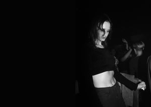 Person wearing a black crop top and dark trousers dancing in a dimly lit setting