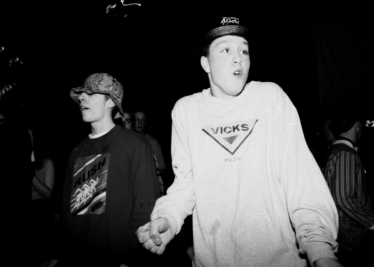 Two people, one wearing a Vicks sweater, standing together in a dark setting.