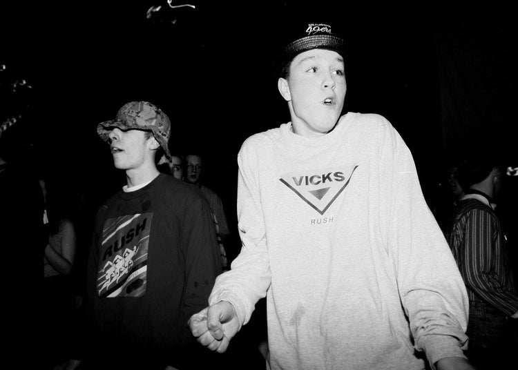 Two people, one wearing a Vicks sweater, standing together in a dark setting.