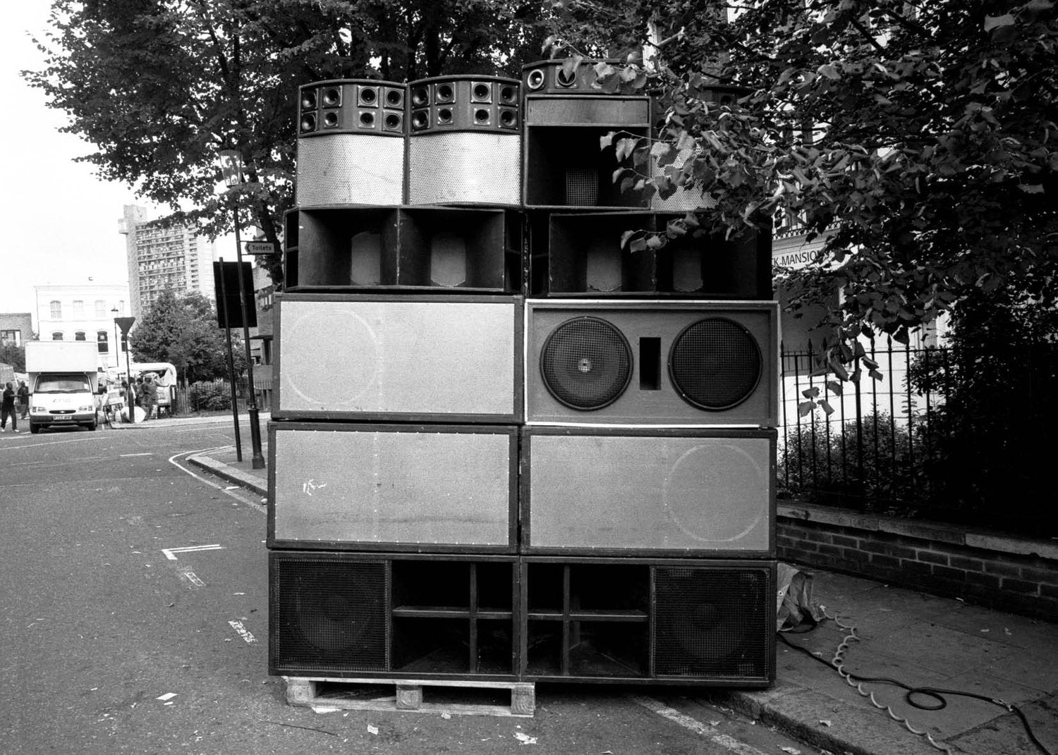 Stack of large speakers on a London street with trees and buildings in the background