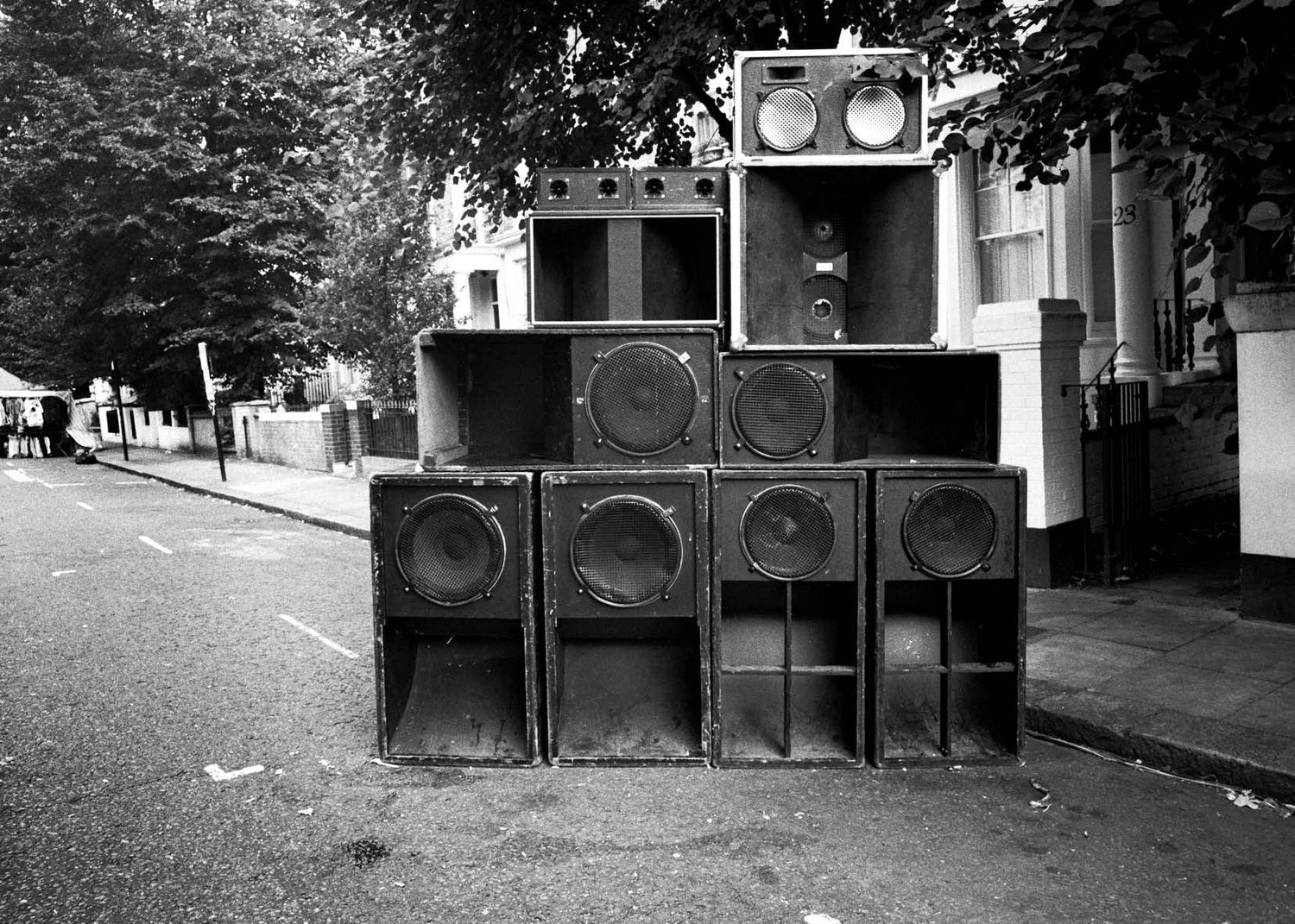 Stack of large speakers on a street in London with trees and buildings in the background