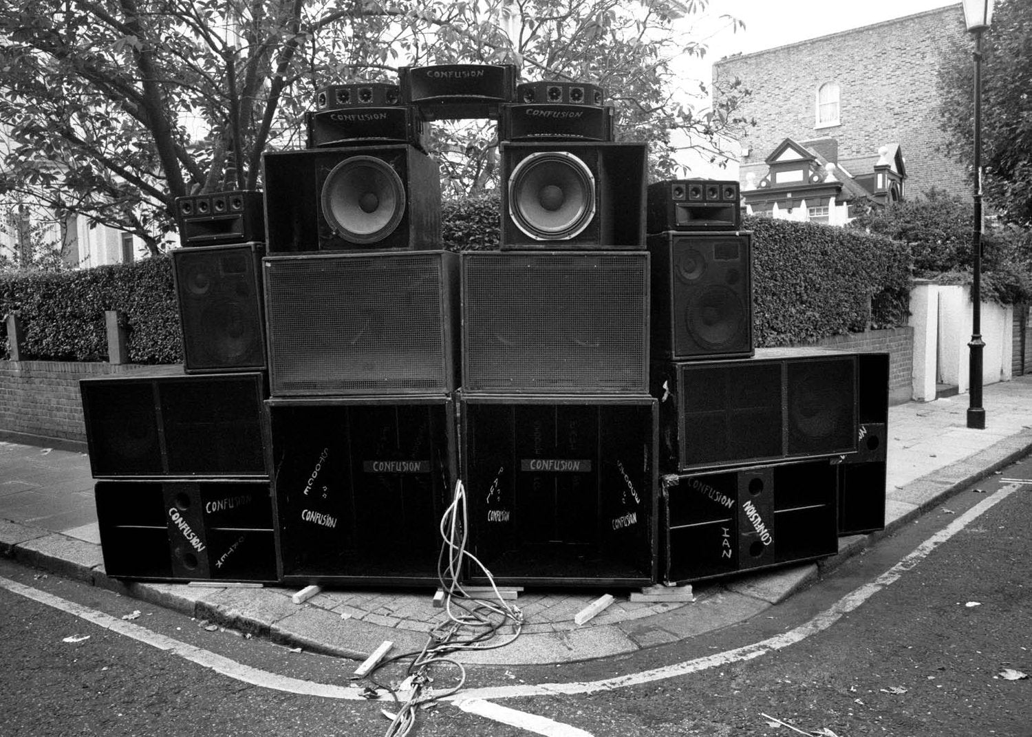Stack of large speakers on a street corner with trees and buildings in the background, Notting Hill, London