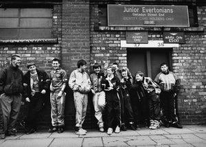Group of young people posing in front of a brick building with a sign for 'Junior Evertonians'.