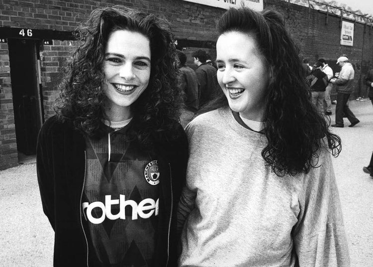 Two female football fans standing together outside a football ground.