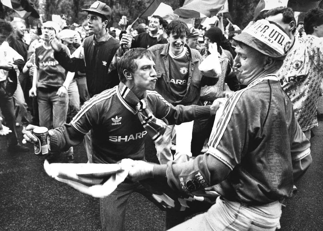 Two men in football jerseys interacting with a crowd of people in a black and white photograph.