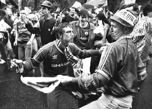 Two men in football jerseys interacting with a crowd of people in a black and white photograph.
