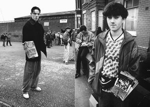 Two football fans standing on a street, holding newspapers, with a crowd in the background.