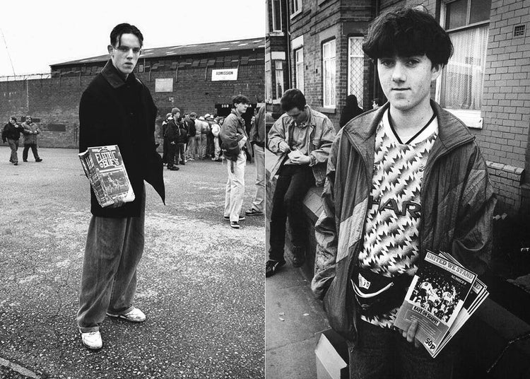 Two football fans standing on a street, holding newspapers, with a crowd in the background.