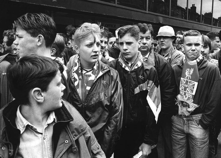 Black and white photo of a group of young people, some wearing football scarves, outside a football ground