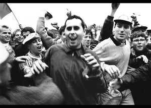 Black and white photo of a crowd of people with one person cheering in the foreground