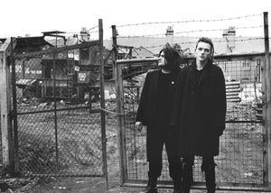 Two people standing in front of a barbed wire fence with building site in the background.