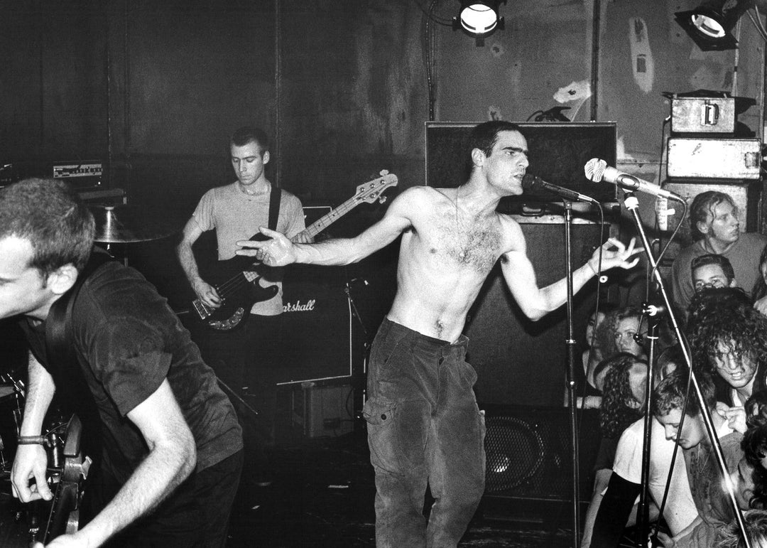 Band performing on stage with a shirtless lead singer and guitarist in background