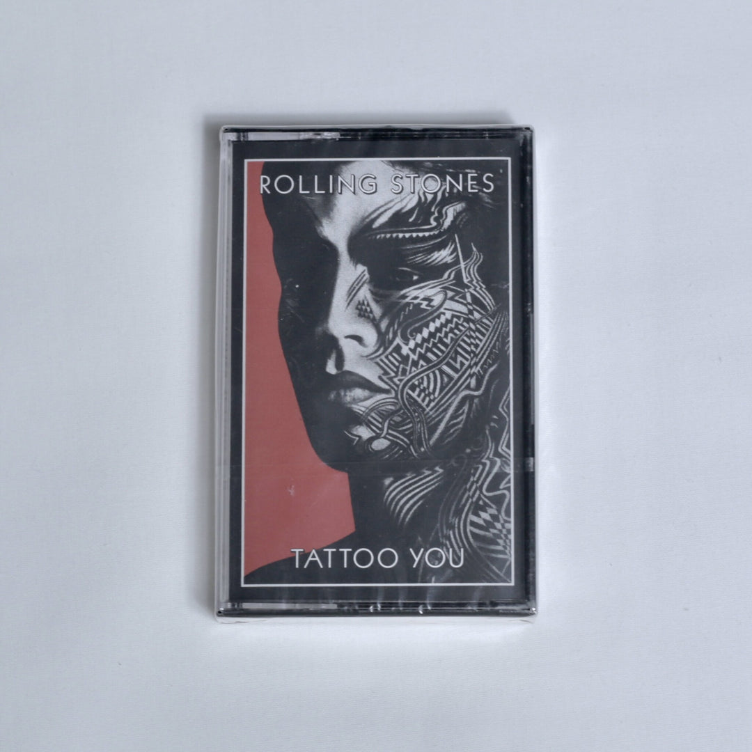 A sealed cassette tape of the band Rolling Stones' album 'Tattoo You', featuring the black and red album cover art, photographed on a light gray background.