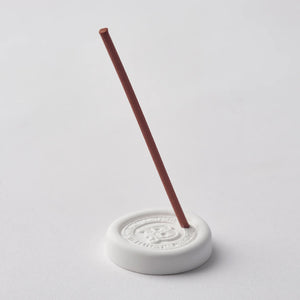 White incense burner with a single red incense stick on a light gray background