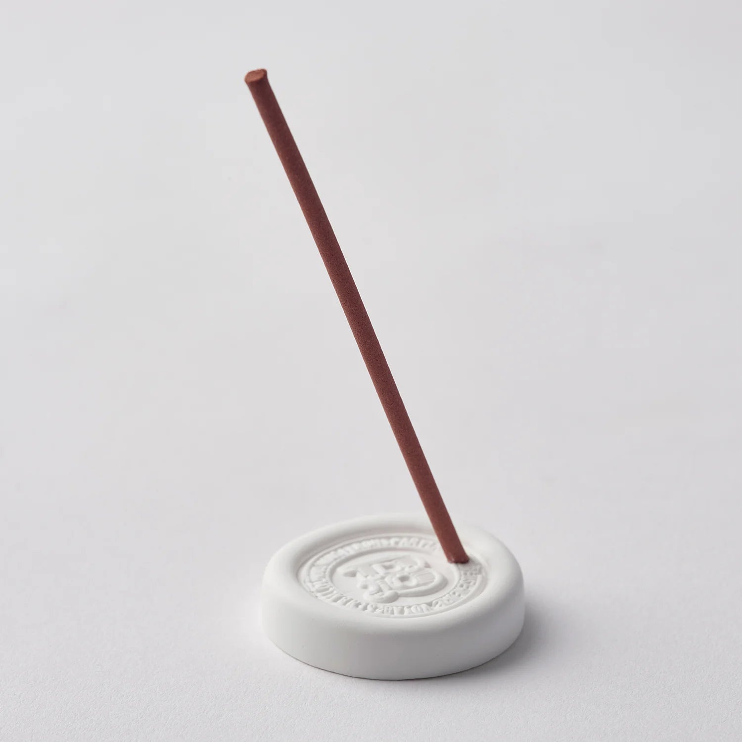 White incense burner with a single red incense stick on a light gray background