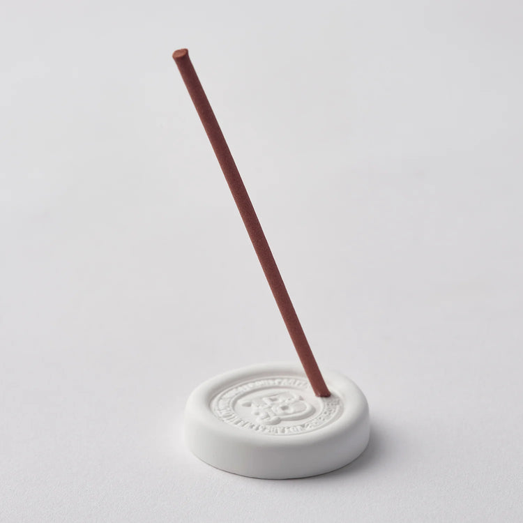 White incense burner with a single red incense stick on a light gray background