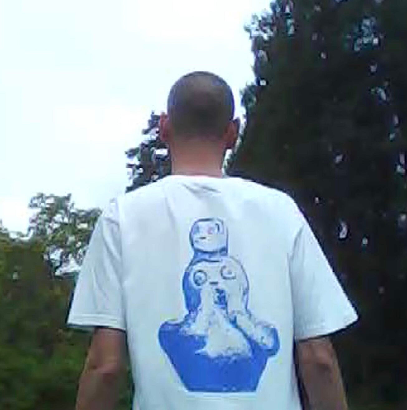 Person wearing a white t-shirt with a robot graphic on the back, standing outdoors.