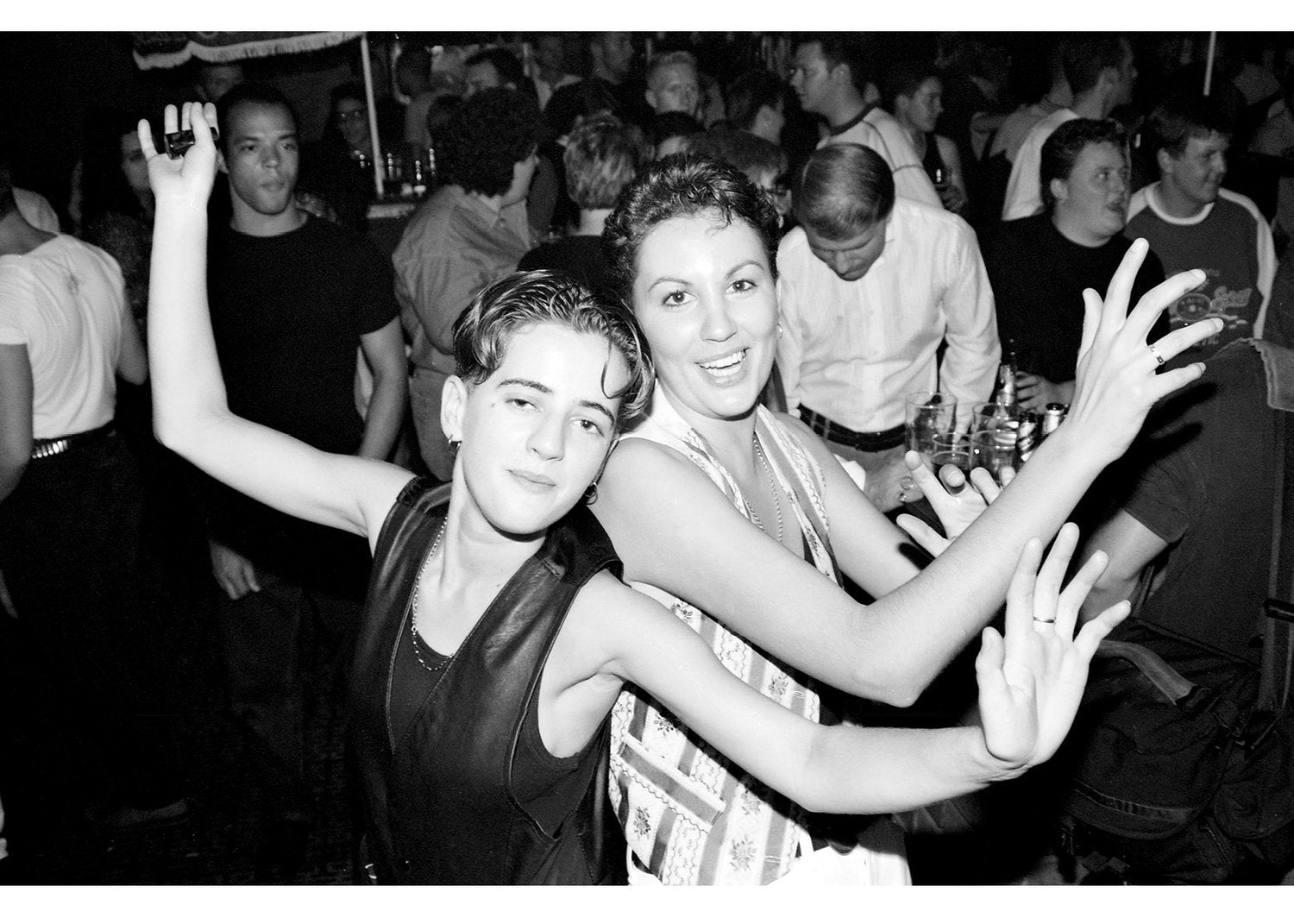 Two people posing together at a club with people in the background.