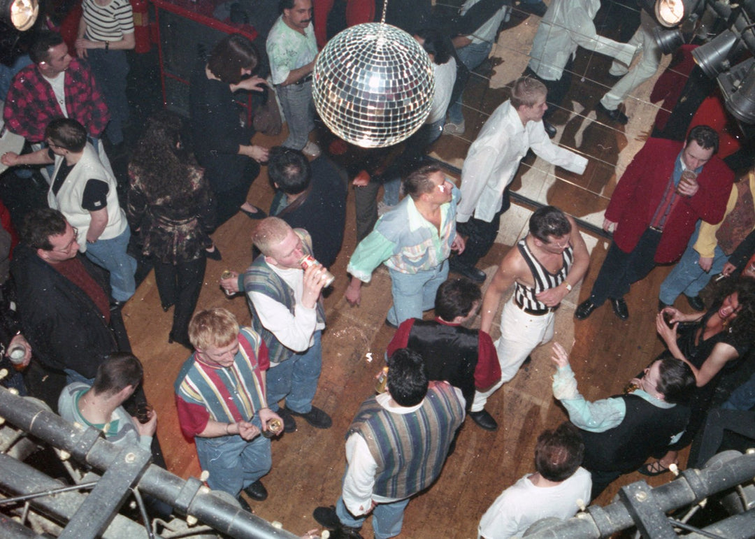 People dancing in a disco setting with a disco ball hanging from the ceiling.