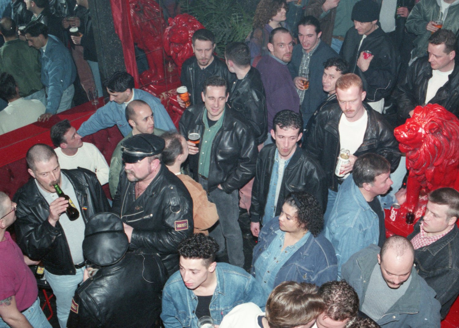 Crowded club with people socialising, drinking, and a red lion statue.