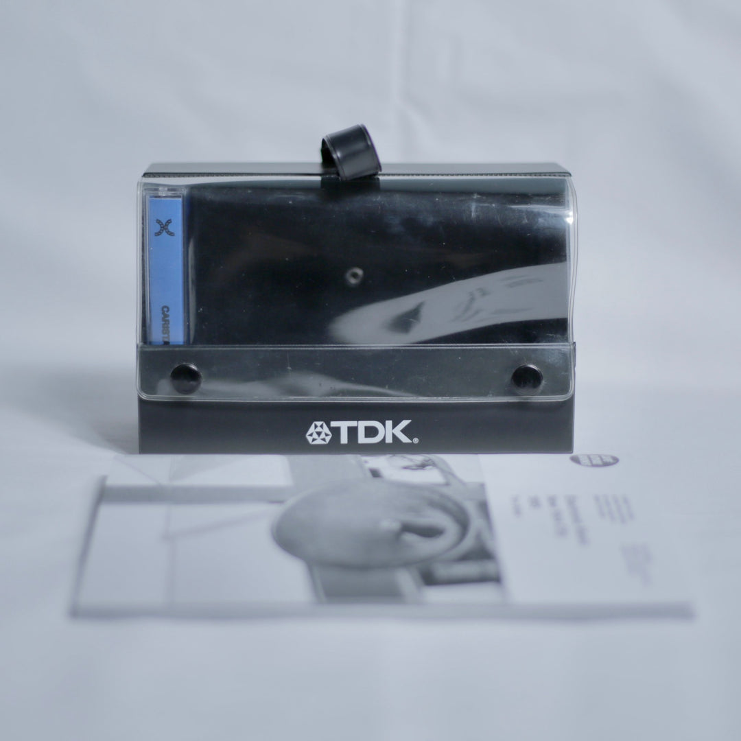 TDK cassette case holding a tape, with a zine out of focus in front.