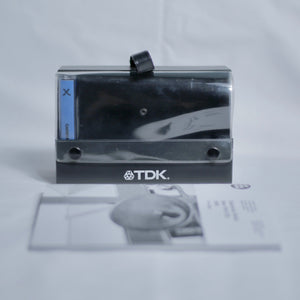TDK cassette case holding a tape, with a zine out of focus in front.
