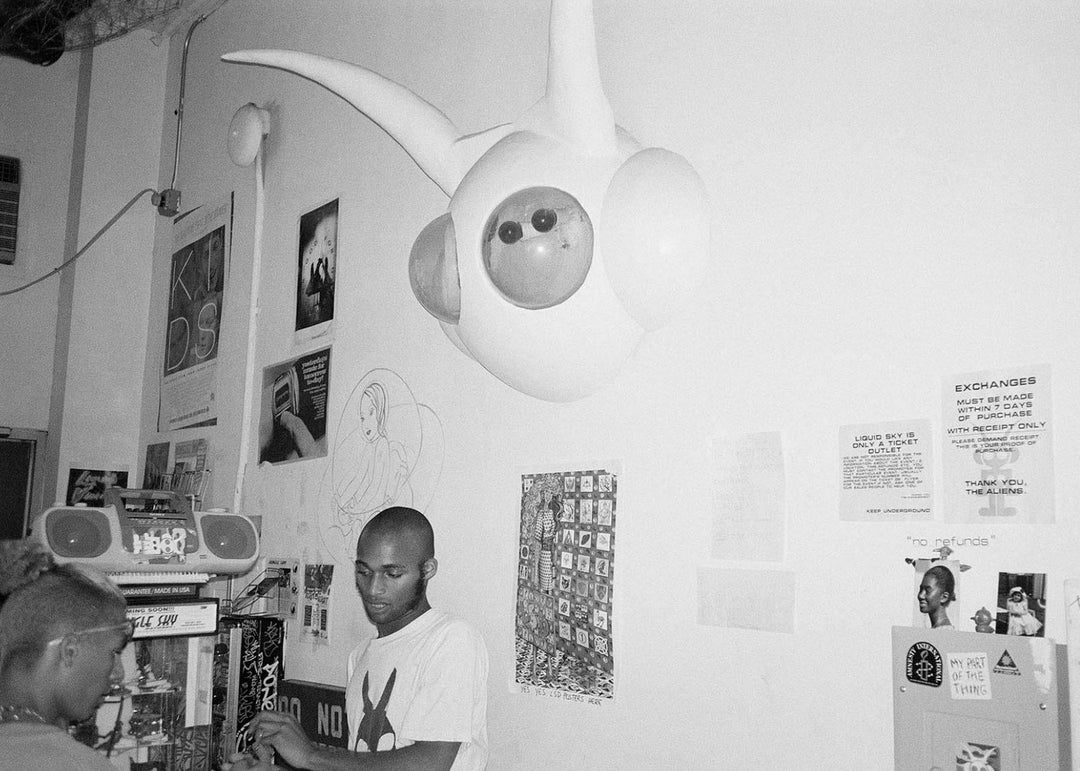 Person standing in a room with a large robot-like creature and posters on the wall.