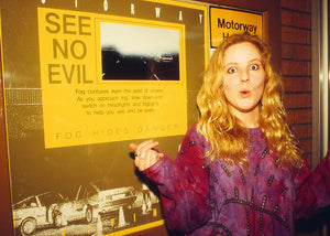 Woman pointing at a 'See No Evil' poster on a motorway.