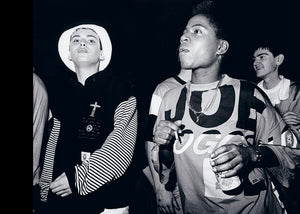 Black and white photo of a group of people, one holding a can wearing a chain, one wearing a white hat.