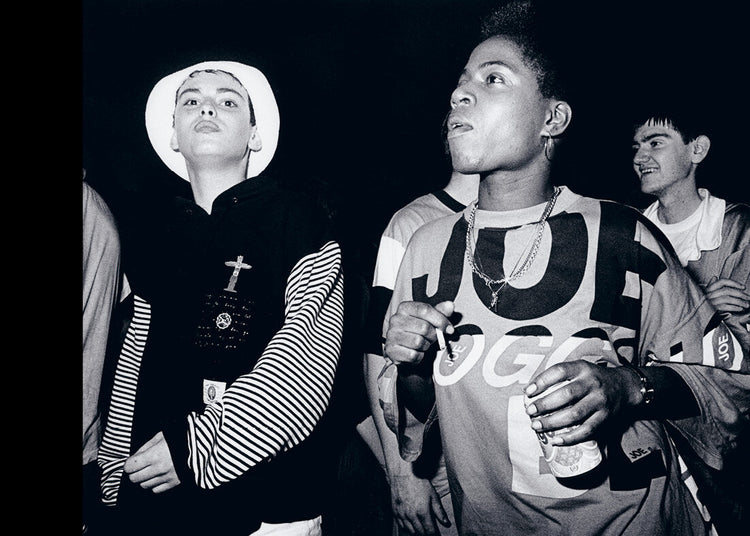 Black and white photo of a group of people, one holding a can wearing a chain, one wearing a white hat.