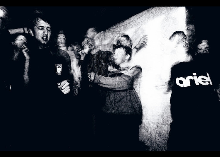 Black and white image of a group of people at rave with one person wearing a 'ariel' shirt.