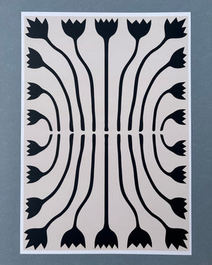 Tilly Worth Tulips A3 print featuring a symmetrical black floral pattern on a light beige background, bordered in white and photographed against a muted blue-grey backdrop.