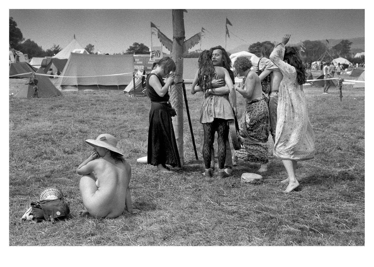 Black and white photograph of people at a festival with tents and open fields in the background